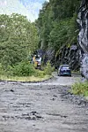Ein grusveg mellom bratte fjellskjeringar, med gravemaskin og bil lenger framme.