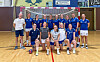 Handballspelarar og trenarar i blå drakter poserer samla i ein idrettshall.