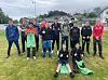 Fotballag poserer samla på ei grasbane med sportsutstyr framfor seg.