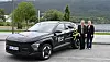 To kvinner står ved ein svart, profilert firmabil på ein parkeringsplass.