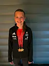 Ung kvinne i svart treningsjakke med to medaljar rundt halsen smiler framfor ein vegg.
